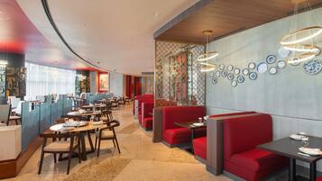 A modern restaurant interior with booths and tables, a patterned wall, and a series of hanging light fixtures.