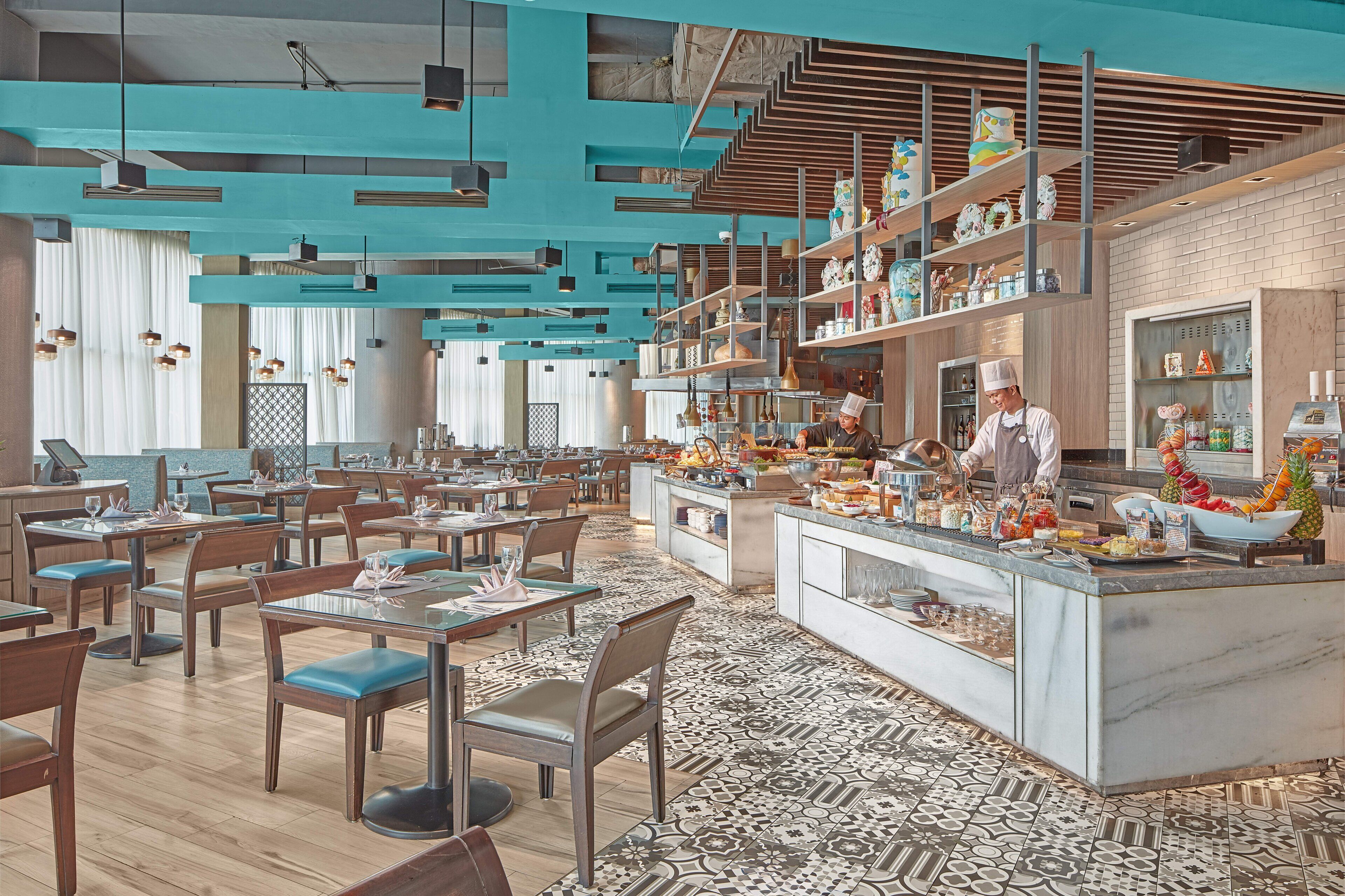 A modern restaurant with wooden tables and chairs, a central island with a chef, and a patterned floor.