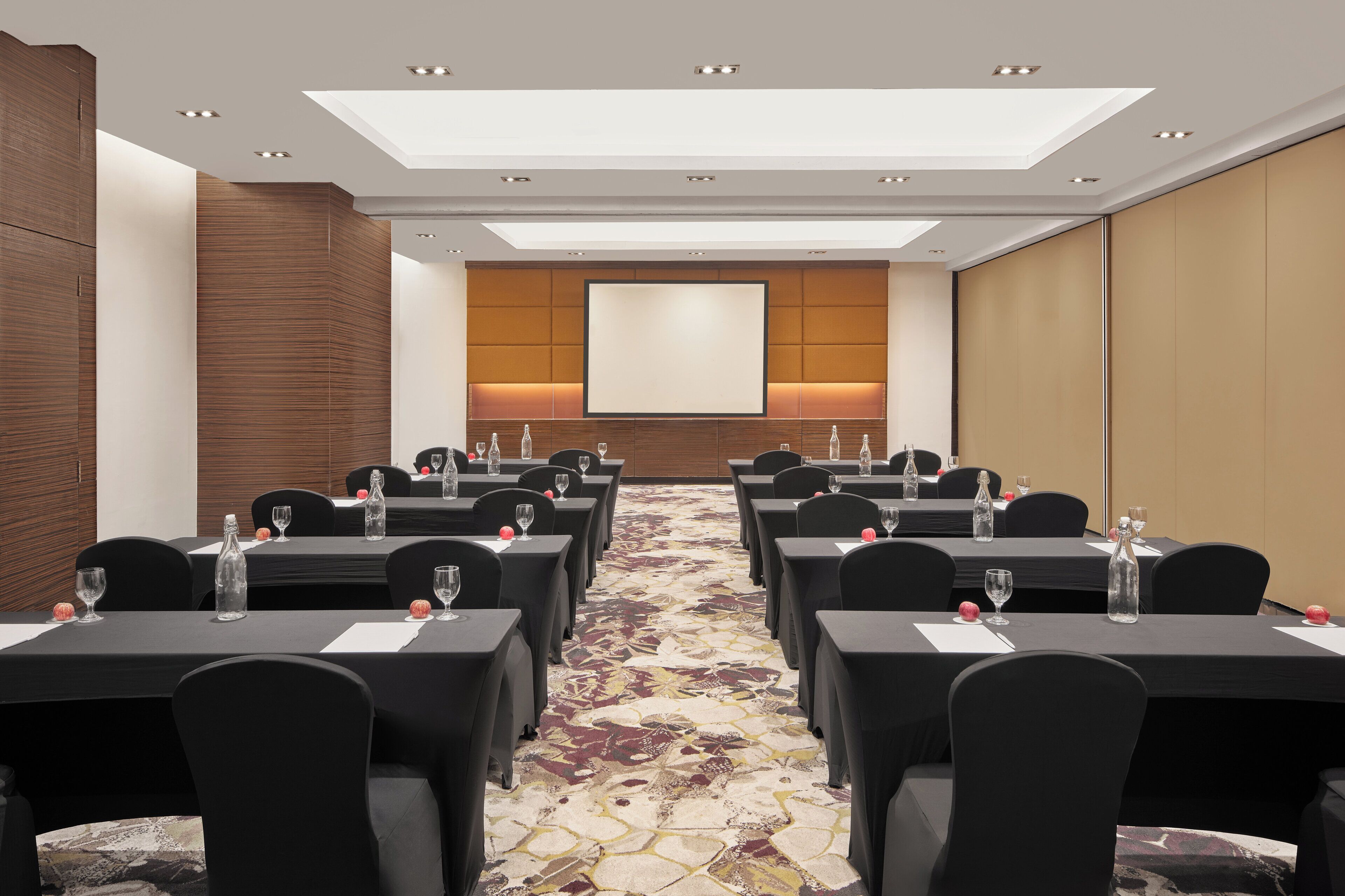 Un salón de conferencias con mesas dispuestas para reuniones, equipado con botellas de agua y vasos.