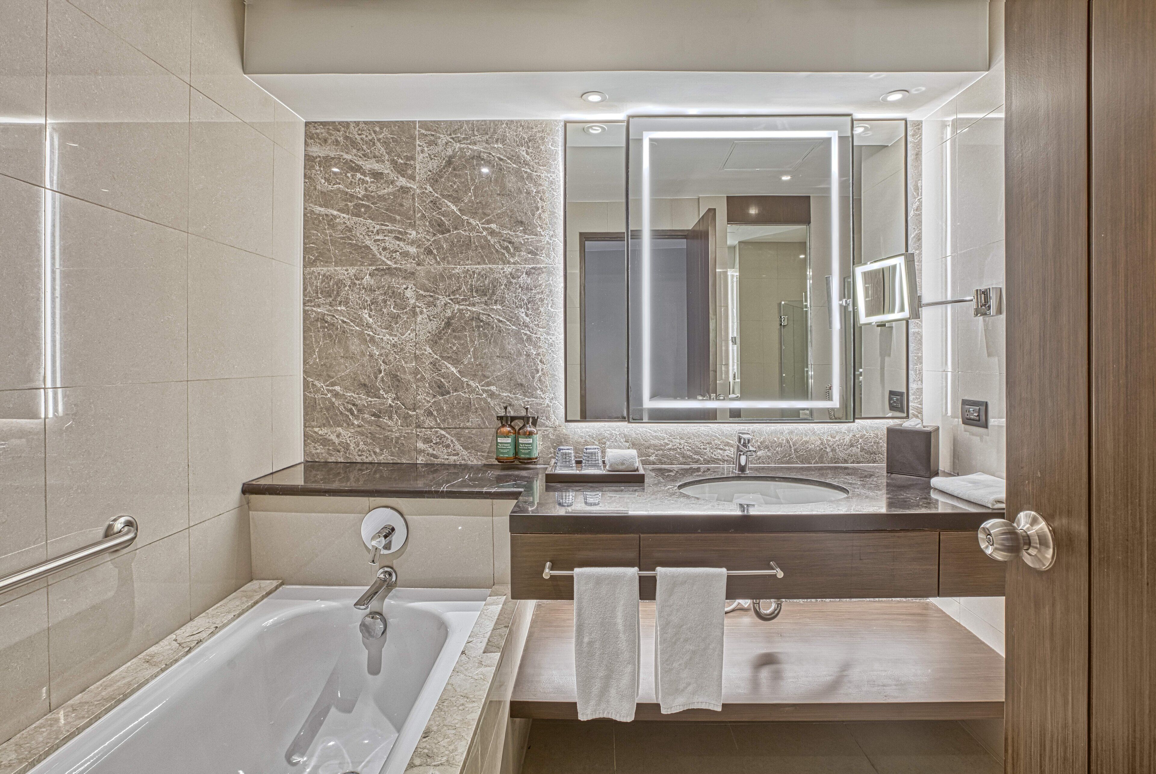 Une salle de bain moderne avec une baignoire, deux lavabos, des murs en marbre et un grand miroir.