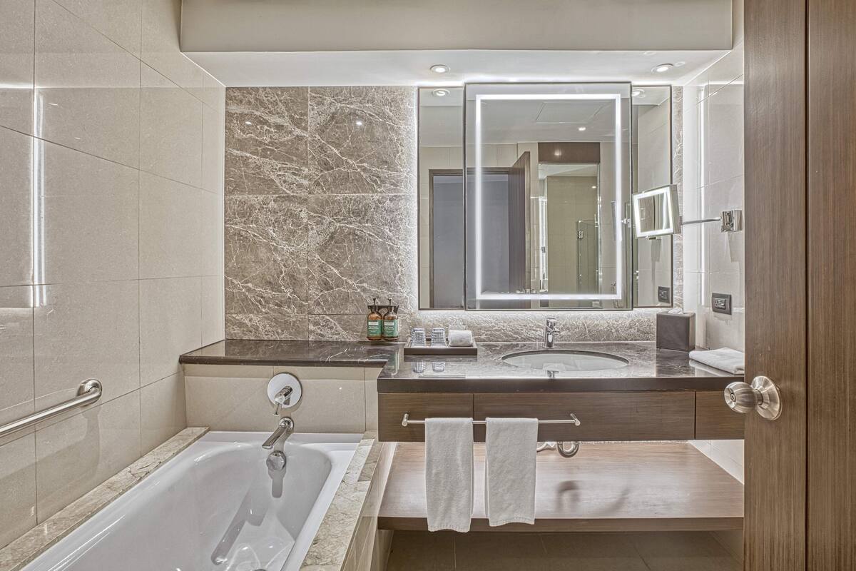 Un baño moderno con bañera, dos lavabos, paredes de mármol y un espejo grande.