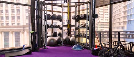 A gym with a purple carpet, weightlifting equipment, and a view of tall buildings.