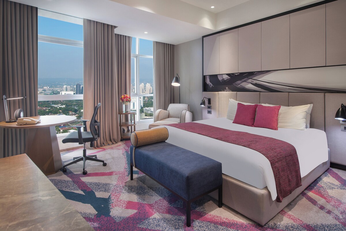 Een moderne hotelkamer met een groot bed, een bureau en uitzicht op een stadsgezicht.