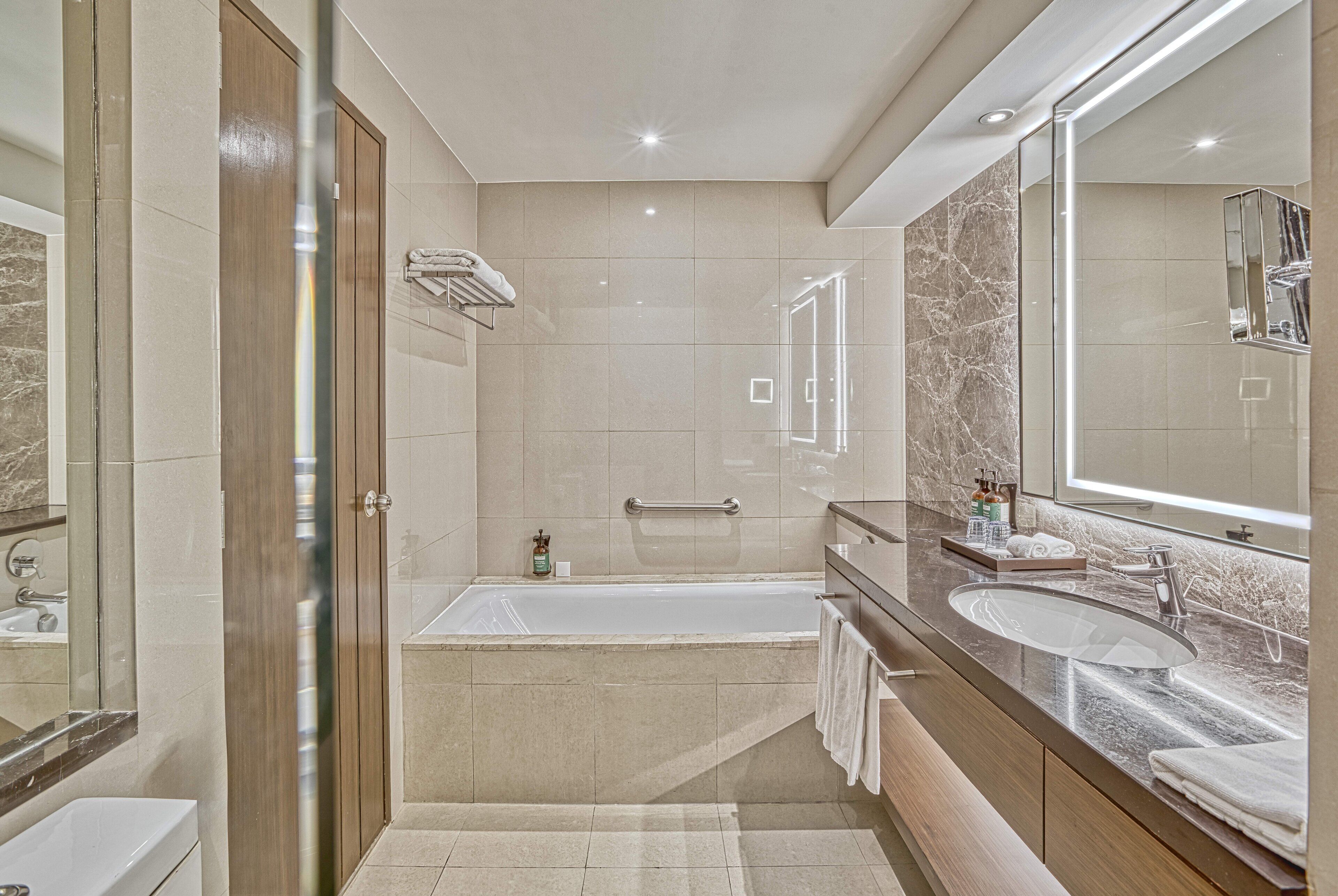 Un baño moderno con bañera, dos lavamanos, un espejo grande y un perchero para toallas.