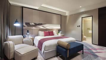 Una habitación de hotel moderna con cama, sofá, banca, escritorio y zona de ducha.