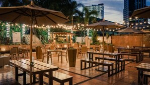 Een terras buiten met houten tafels en stoelen, lichtjes en parasols.