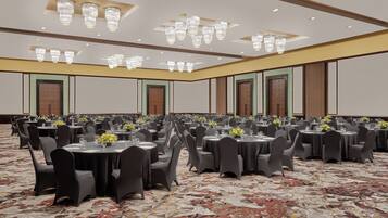 A large banquet hall with round tables, black chairs, and chandeliers.