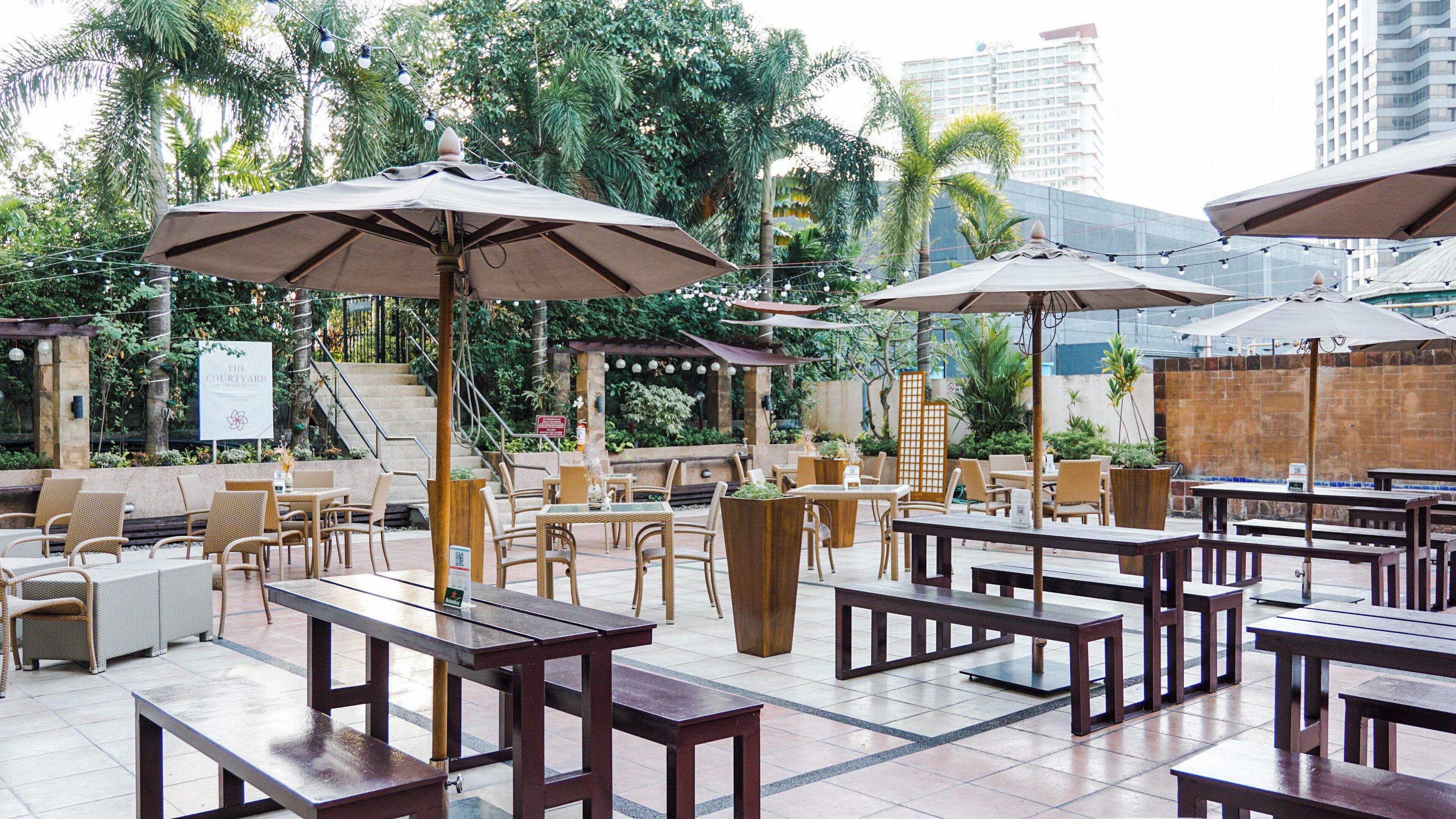 Un espace extérieur aménagé avec des tables et des chaises, des parasols et un escalier menant à un niveau supérieur.