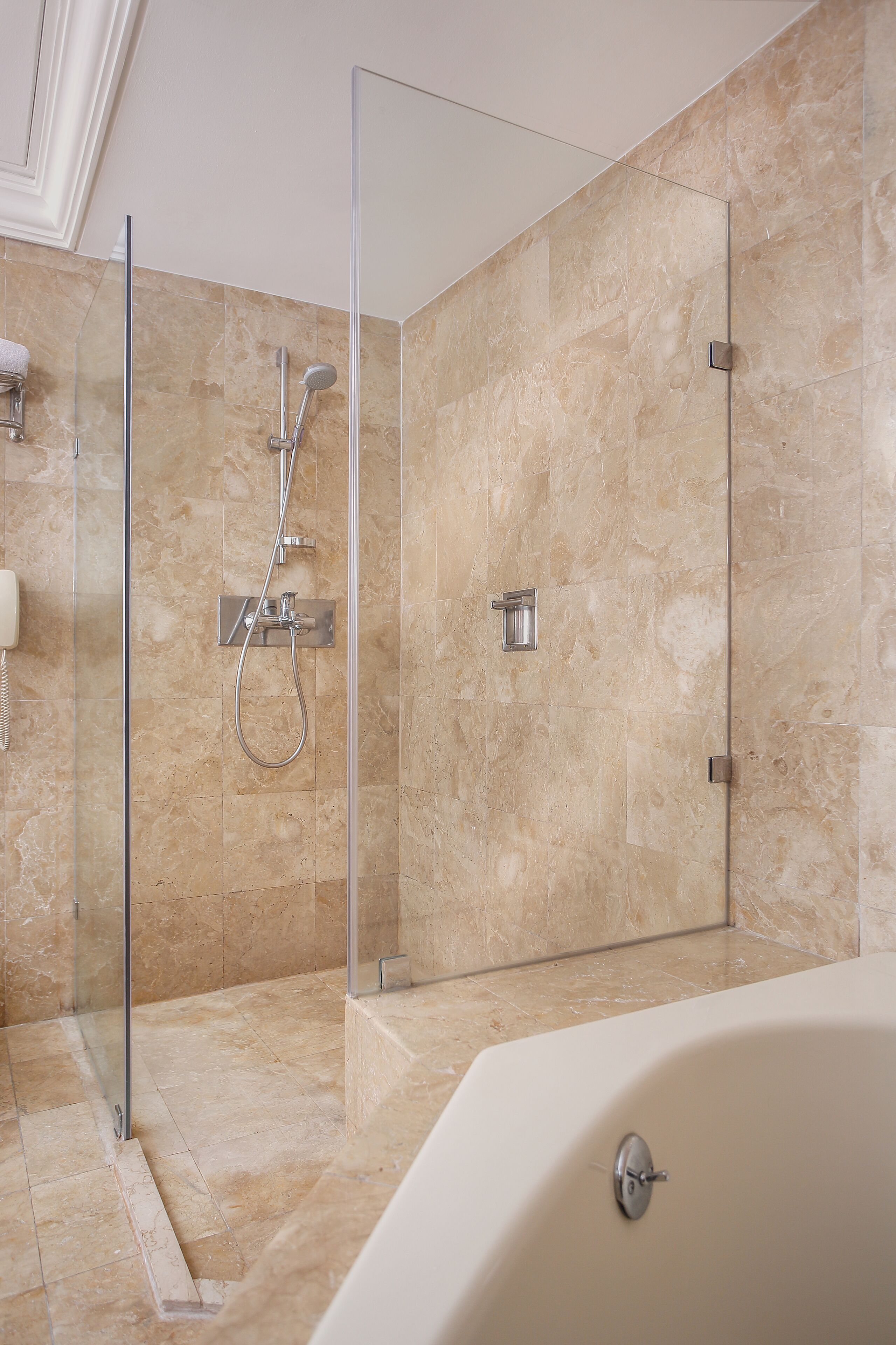 A modern bathroom with a glass-enclosed shower, a bathtub, and marble flooring.