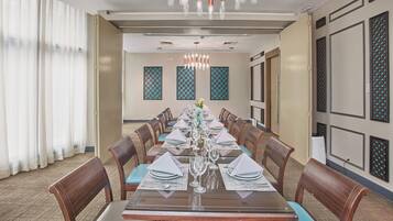 A conference room with a long table set for a meeting, surrounded by chairs, with patterned wall decorations and a chandelier.