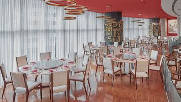 Un vaste espace dédié à la salle à manger, avec des tables rondes, des chaises et un éclairage moderne suspendu au plafond.