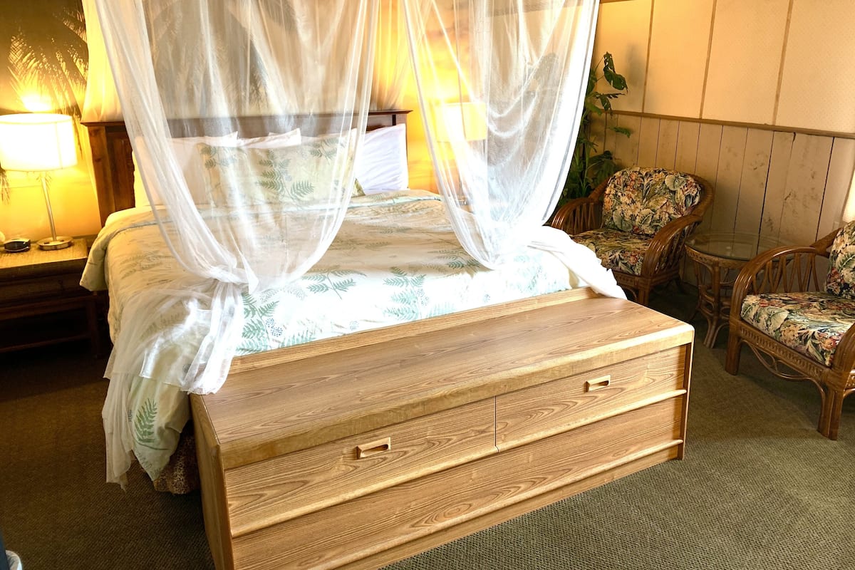 A bed with a canopy, wooden nightstands, a chair, and a lamp.