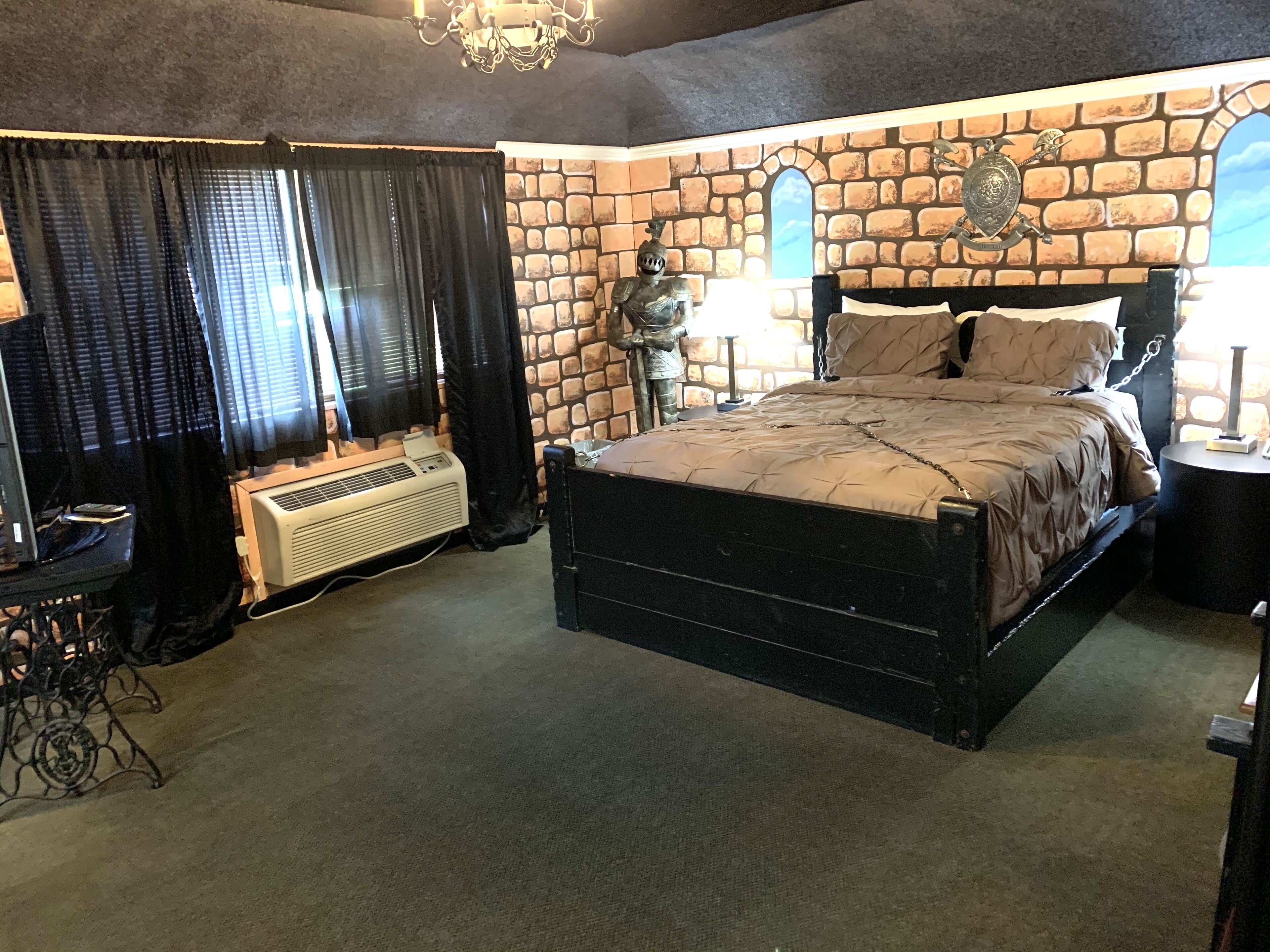 A bedroom with a stone wall, a bed, a heater, and a chandelier.