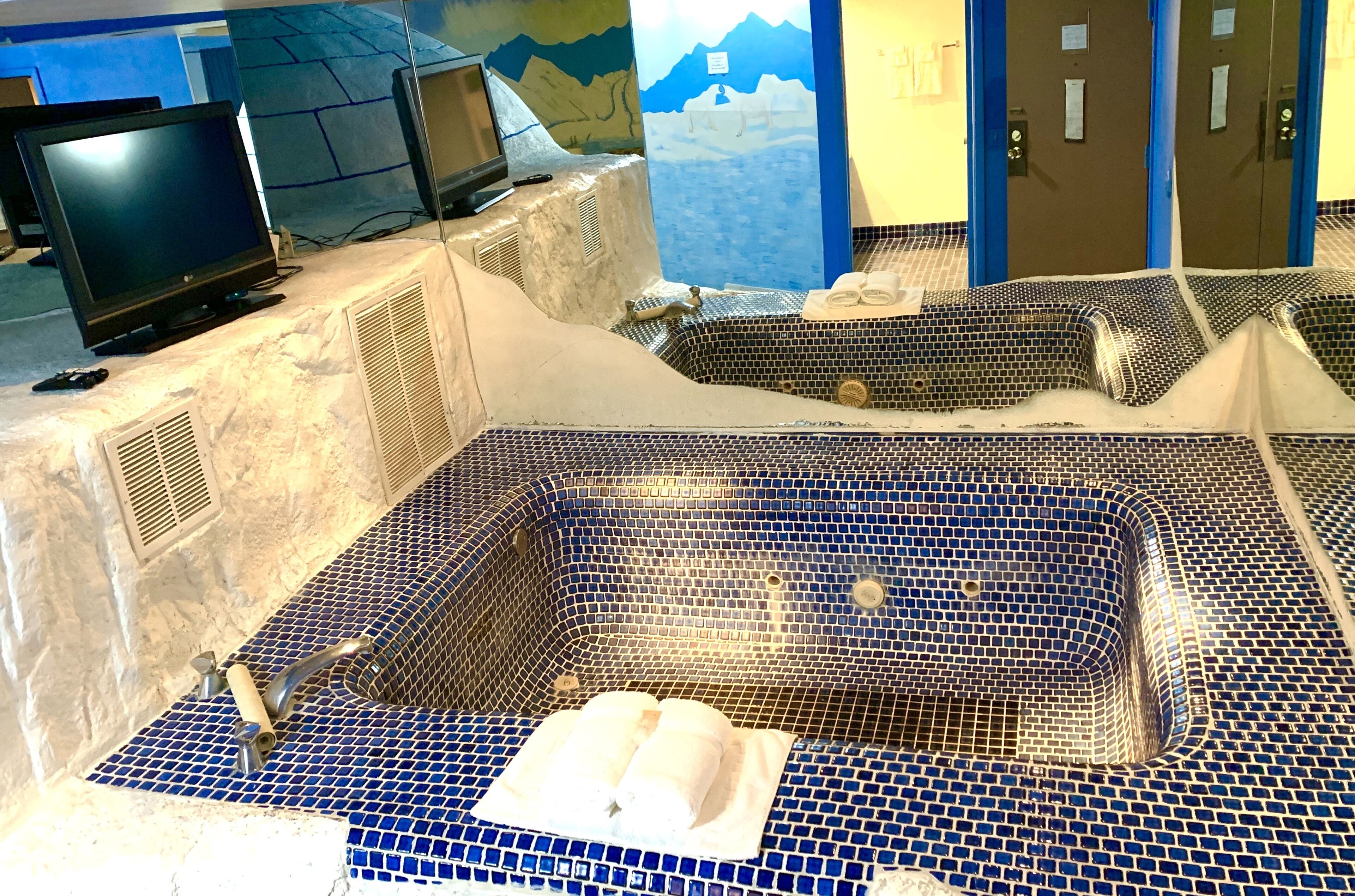 A spa area with a large blue-tiled hot tub, a television, and a mountainous mural on the wall.