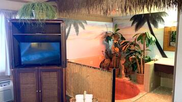 Habitación con televisión, techo de paja, mural con motivos tropicales y una pequeña zona de piscina.