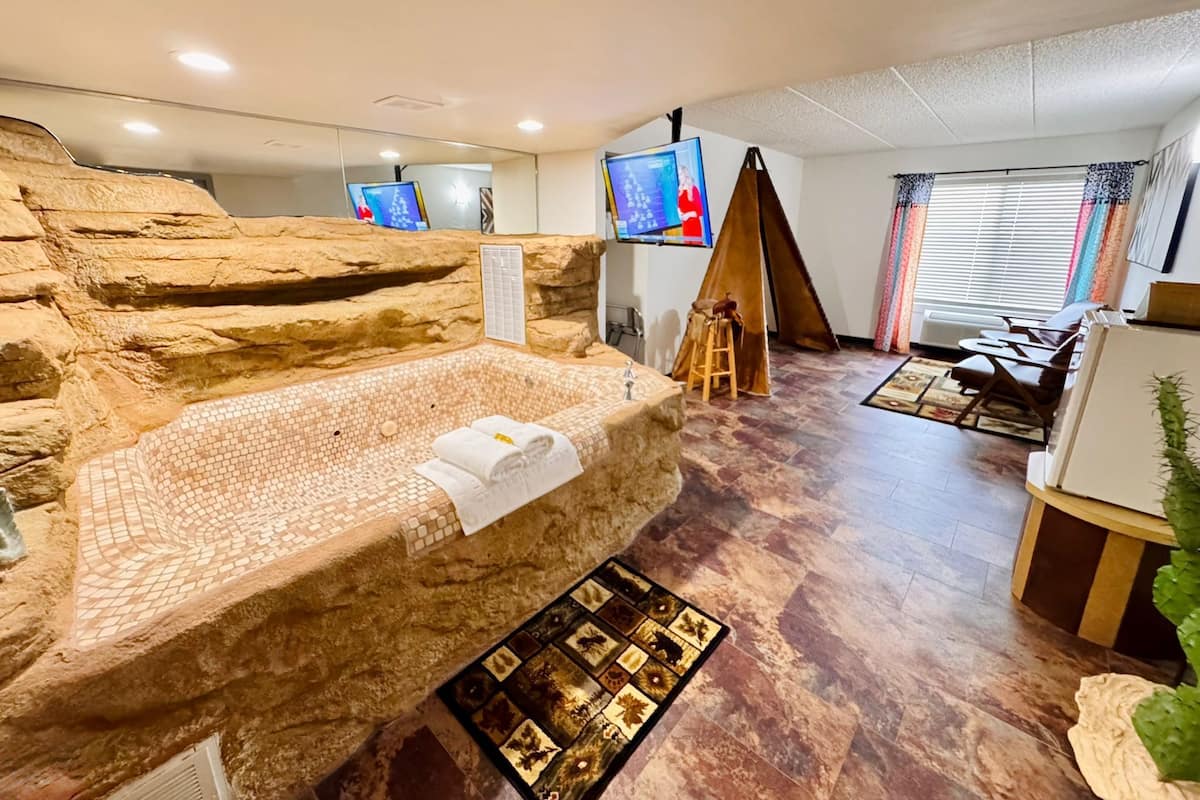 A spa room with a large stone bathtub, a wooden stool, and a television screen.