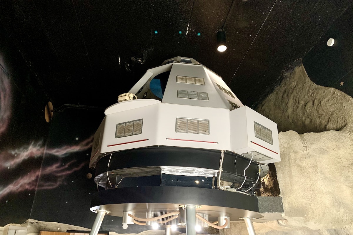 A model of a space station with a hexagonal structure, mounted on a platform with a snowy landscape backdrop.