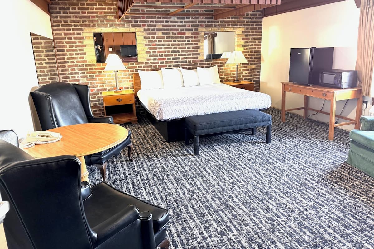 A hotel room with a brick wall, a bed with white bedding, a wooden desk, a television, and a microwave.