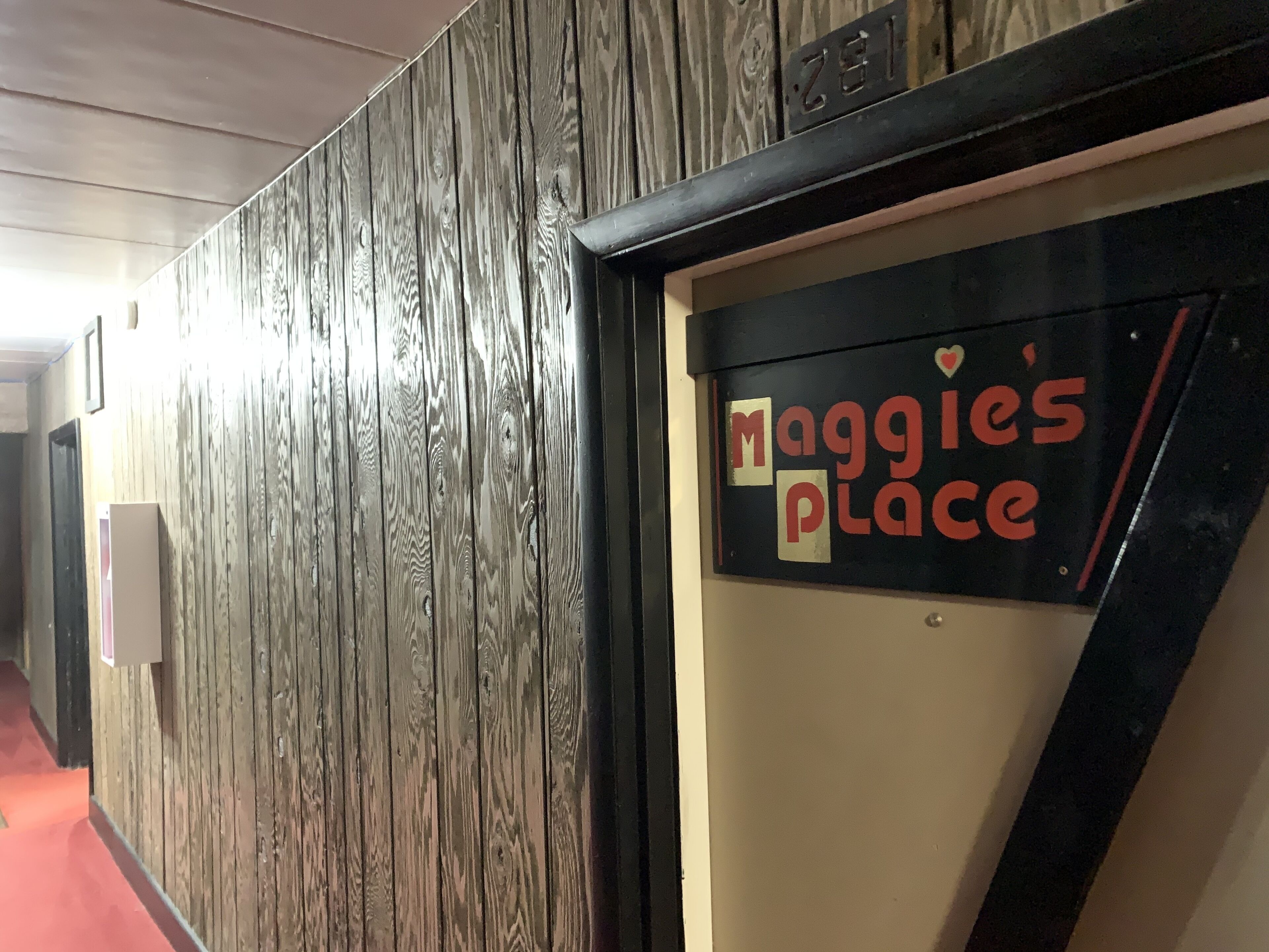 En gang med en trævæg og et skilt med teksten "Maggie's Place".