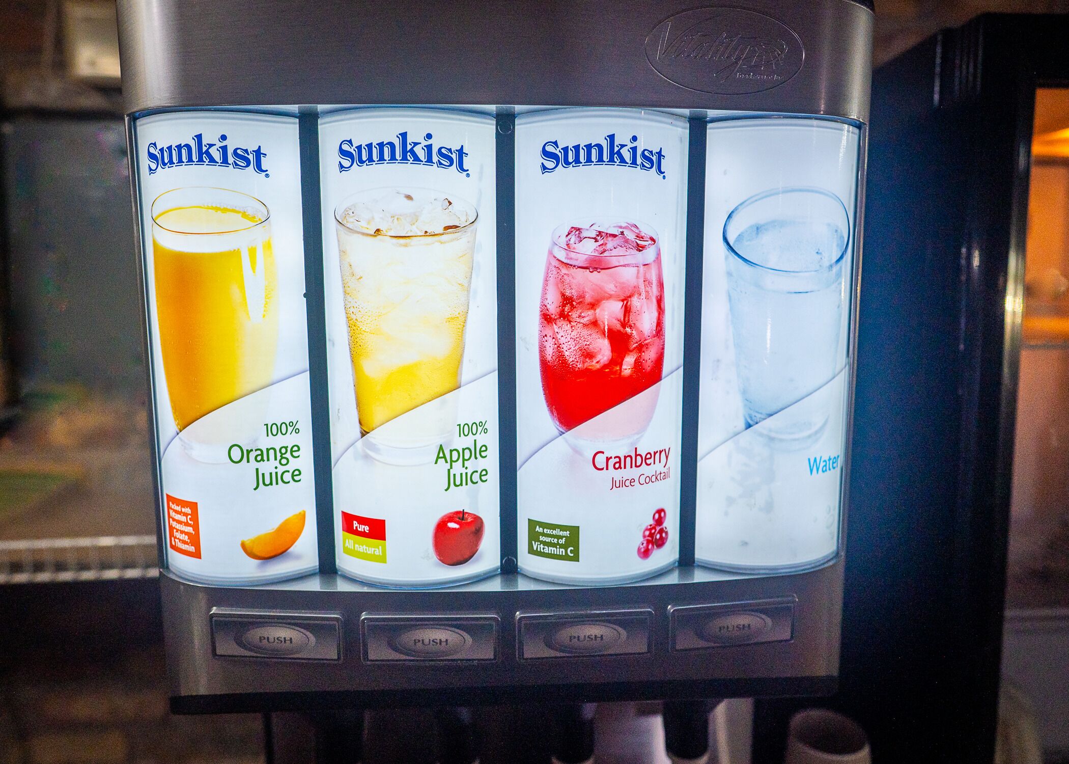 A beverage dispenser with four options: orange juice, apple juice, cranberry juice cocktail, and water.