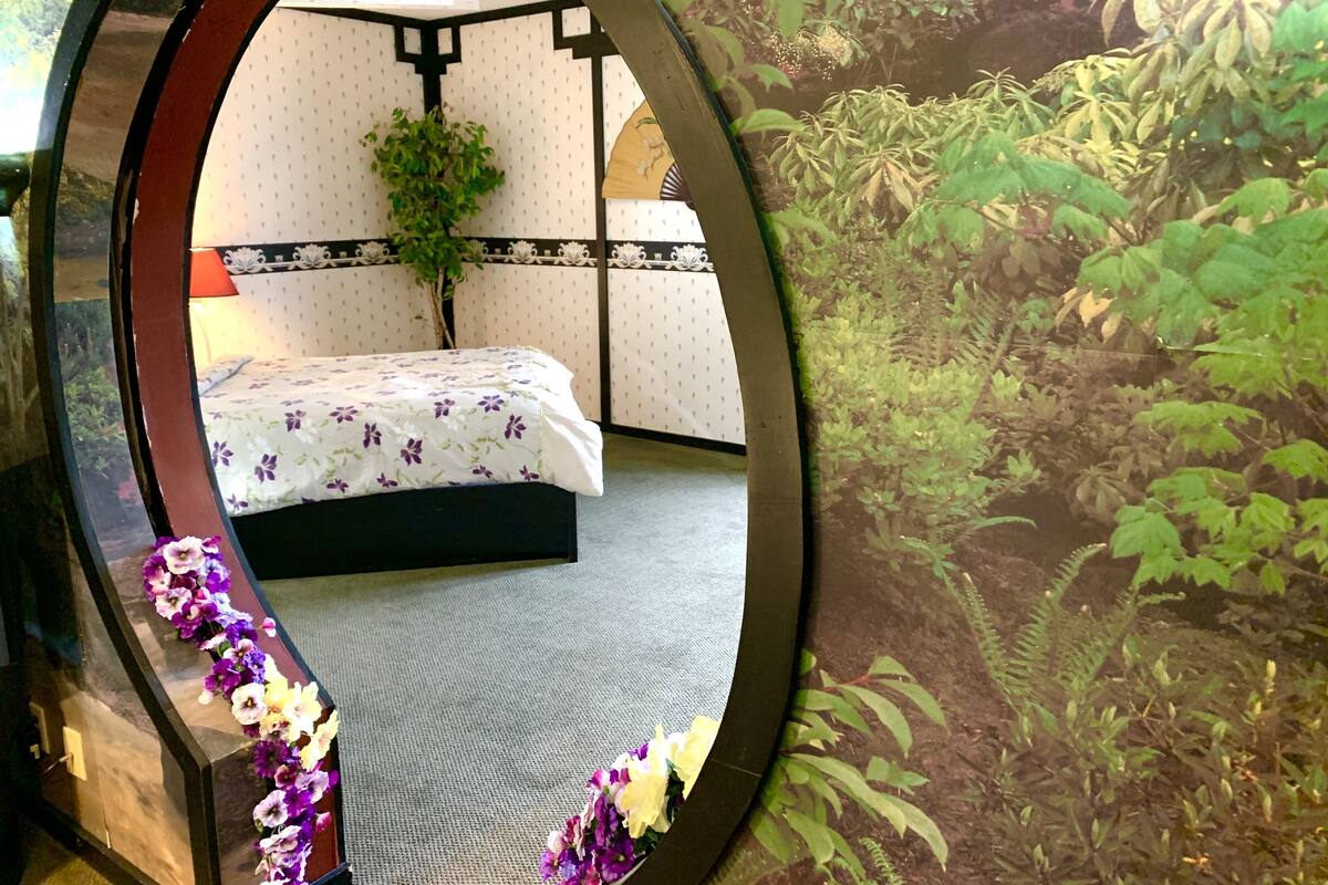 A circular mirror reflecting a bedroom with a bed, a hanging plant, and a patterned wall.