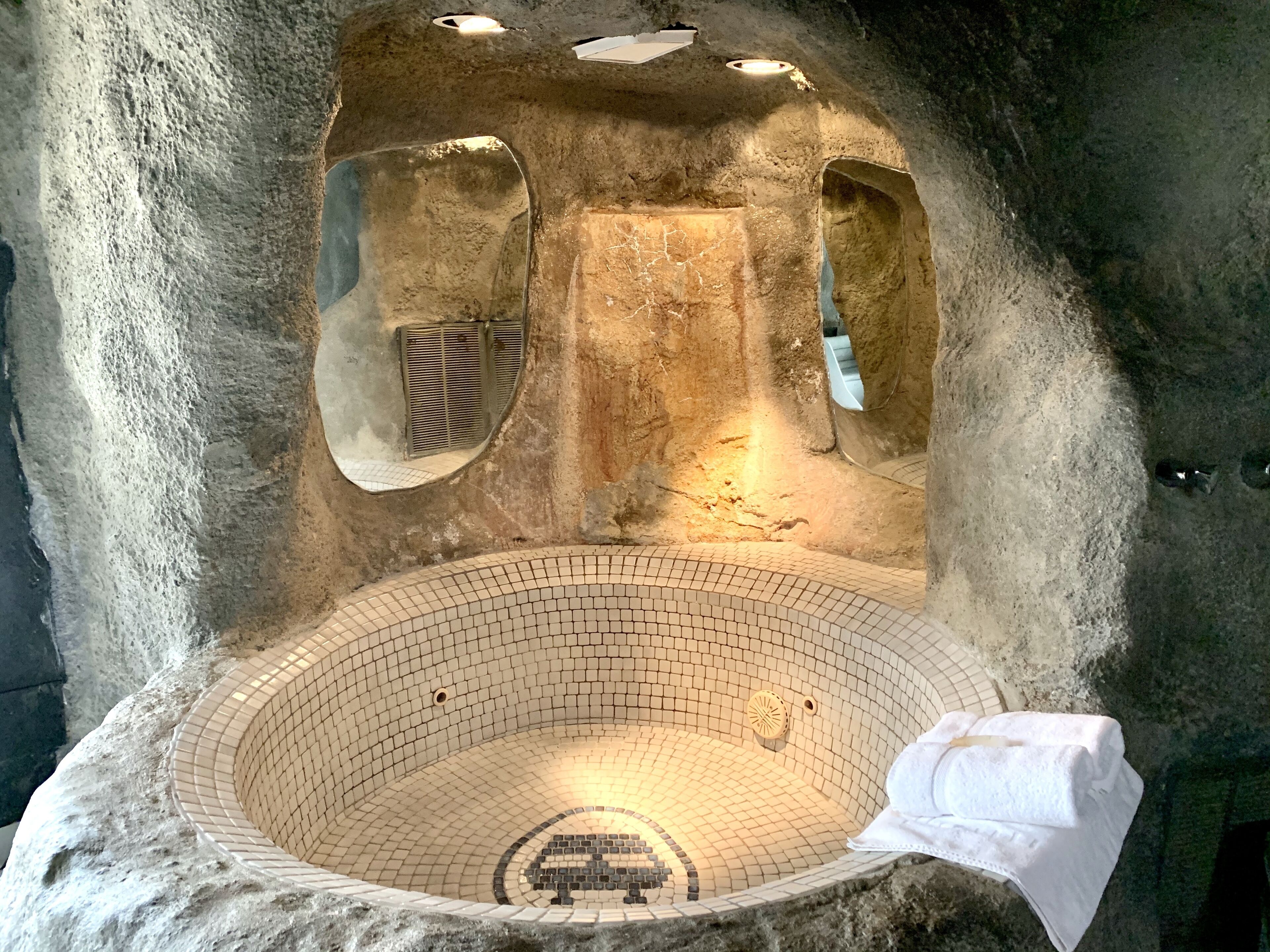 An indoor stone bath with a tiled floor and a white towel.