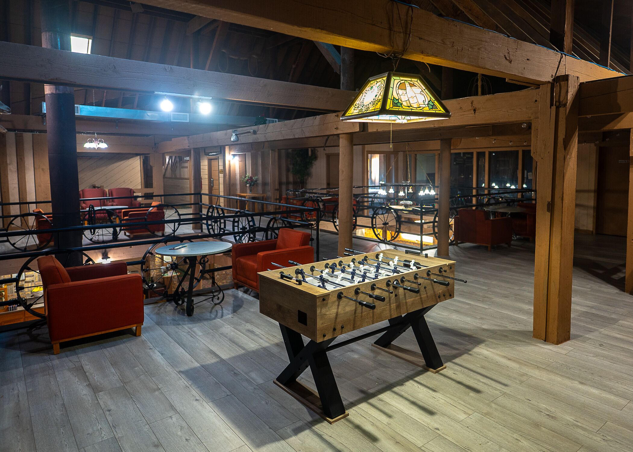 A spacious indoor area with wooden beams, tables, chairs, and a foosball table.