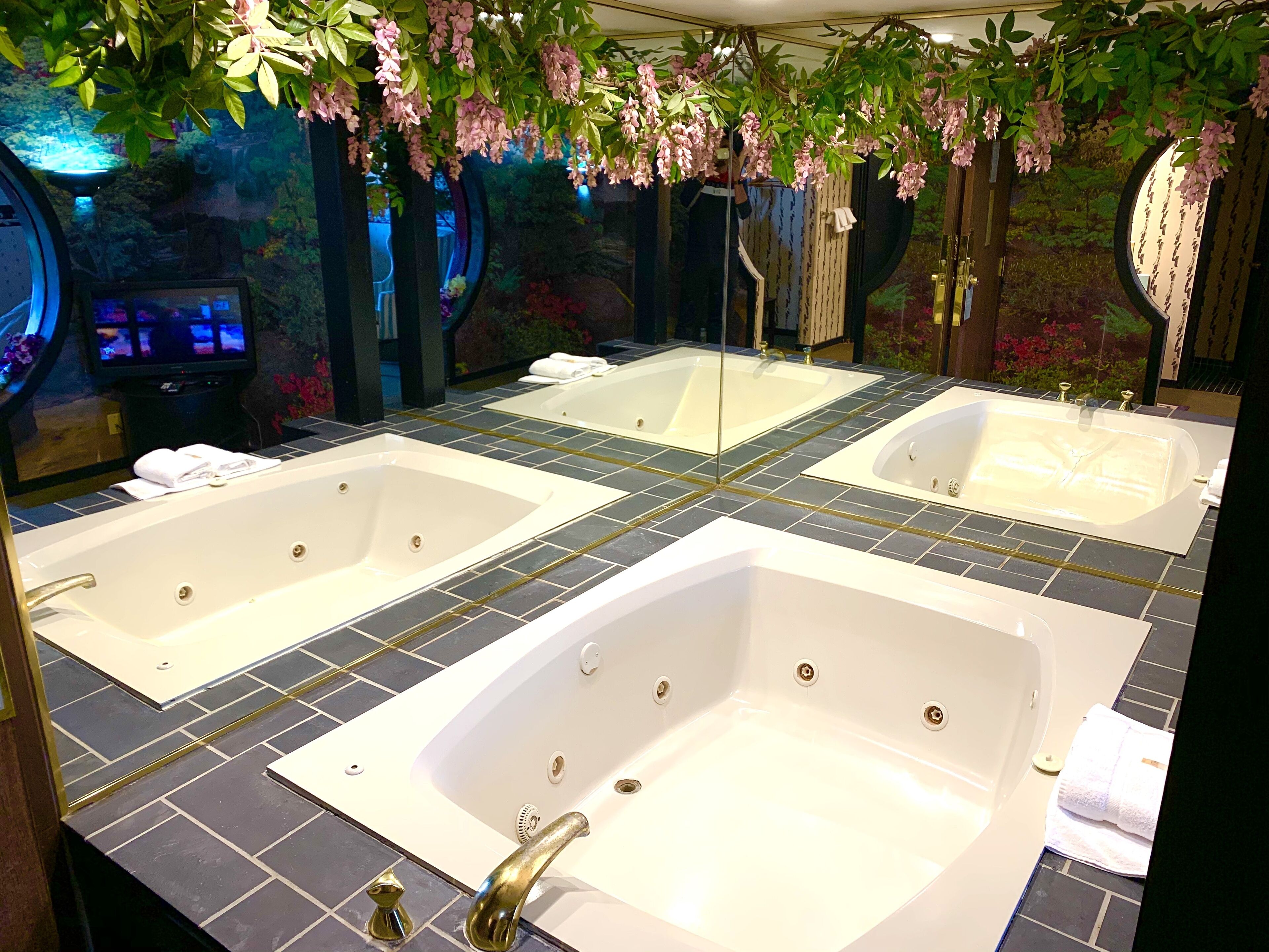 Un bagno con due vasche da bagno bianche, uno specchio e uno schermo televisivo.