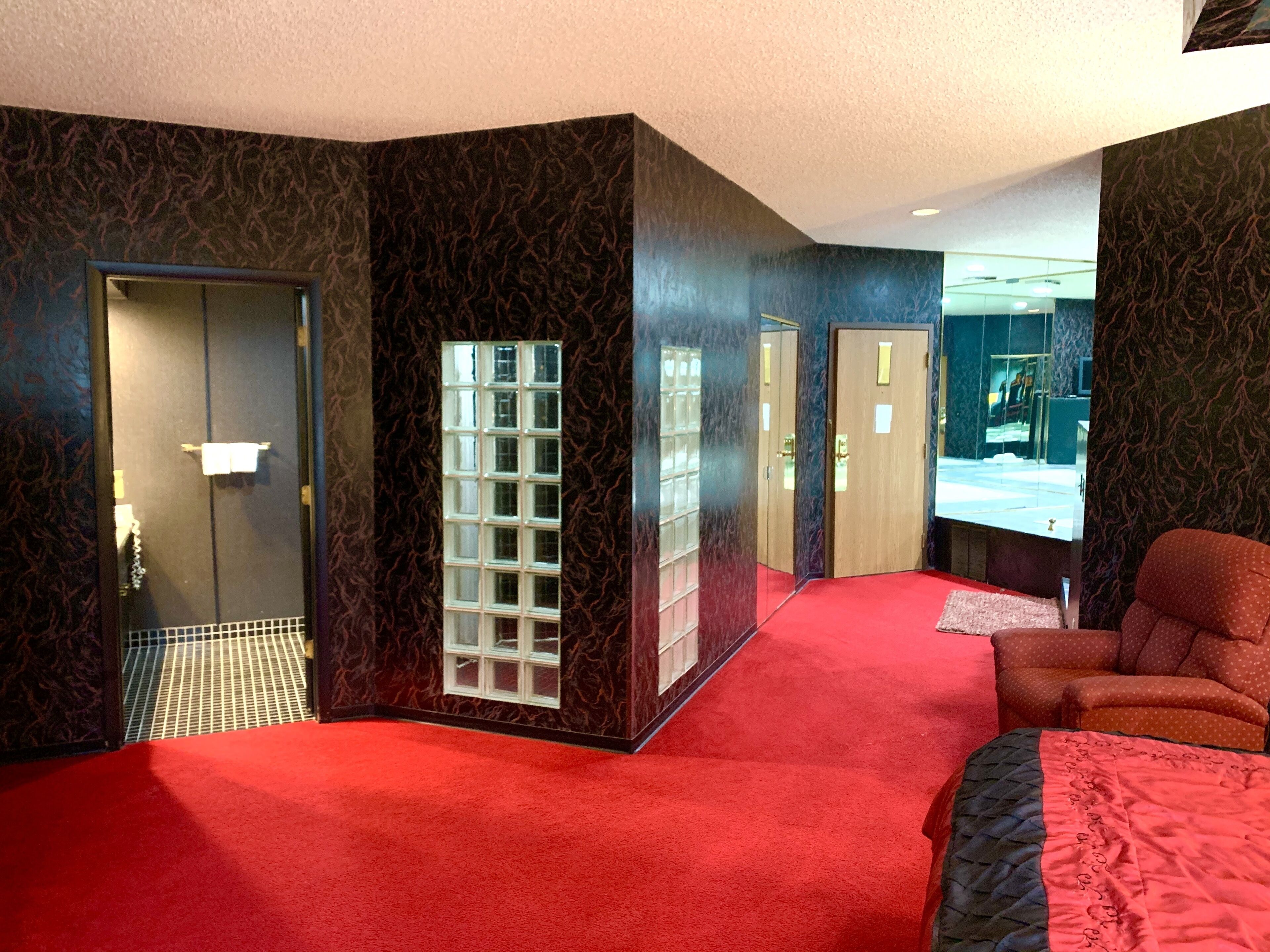 Una habitación de hotel con alfombra roja, una cama grande, un espejo y una puerta que da a un baño.