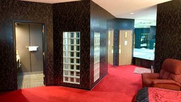 Una habitación de hotel con alfombra roja, una cama grande, un espejo y una puerta que da a un baño.