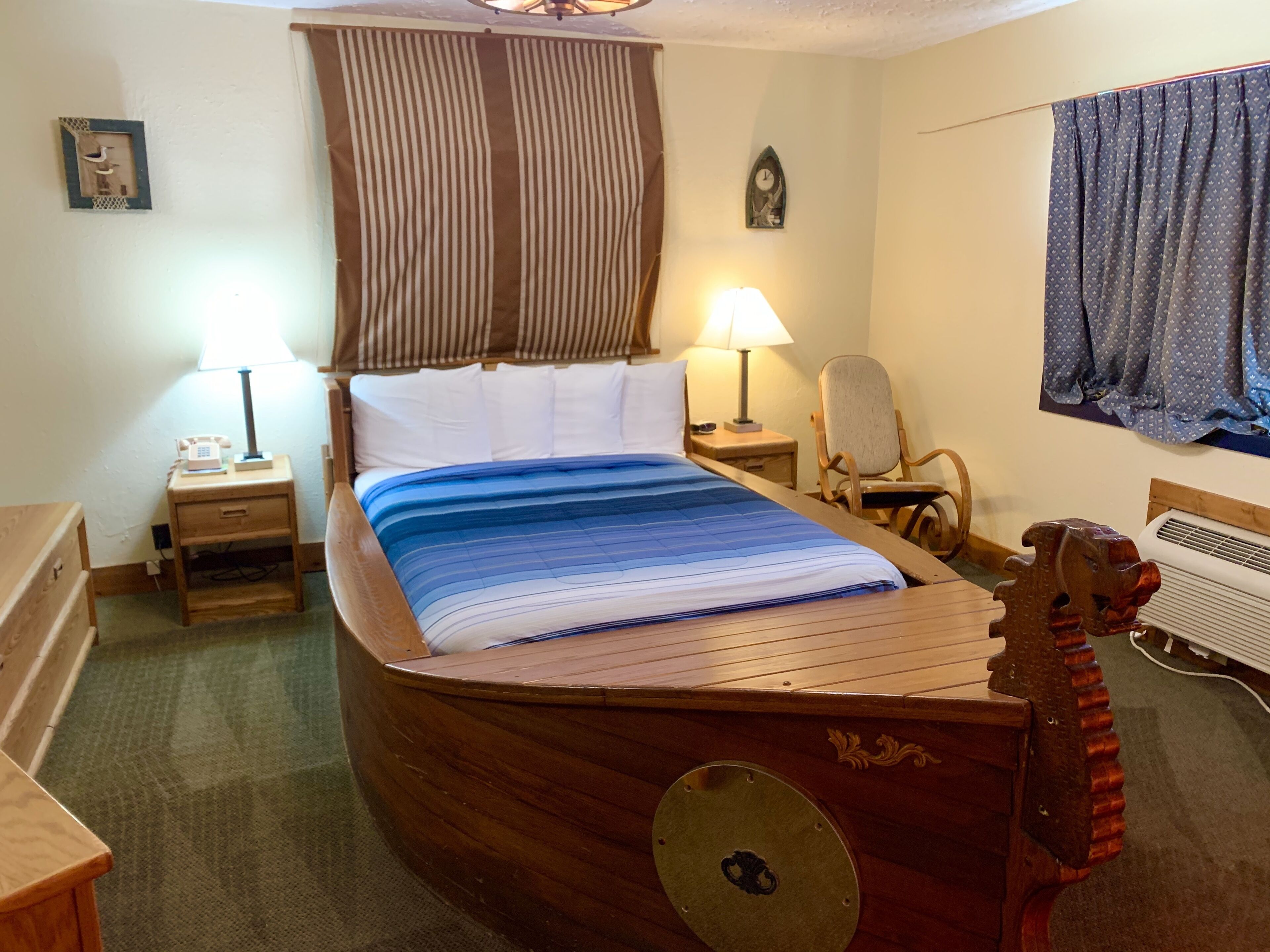 A uniquely shaped wooden bed in a room with a small desk, chair, and a wall clock.