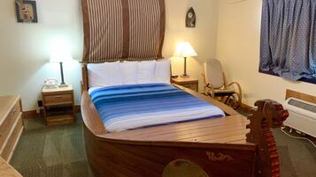 A uniquely shaped wooden bed in a room with a small desk, chair, and a wall clock.