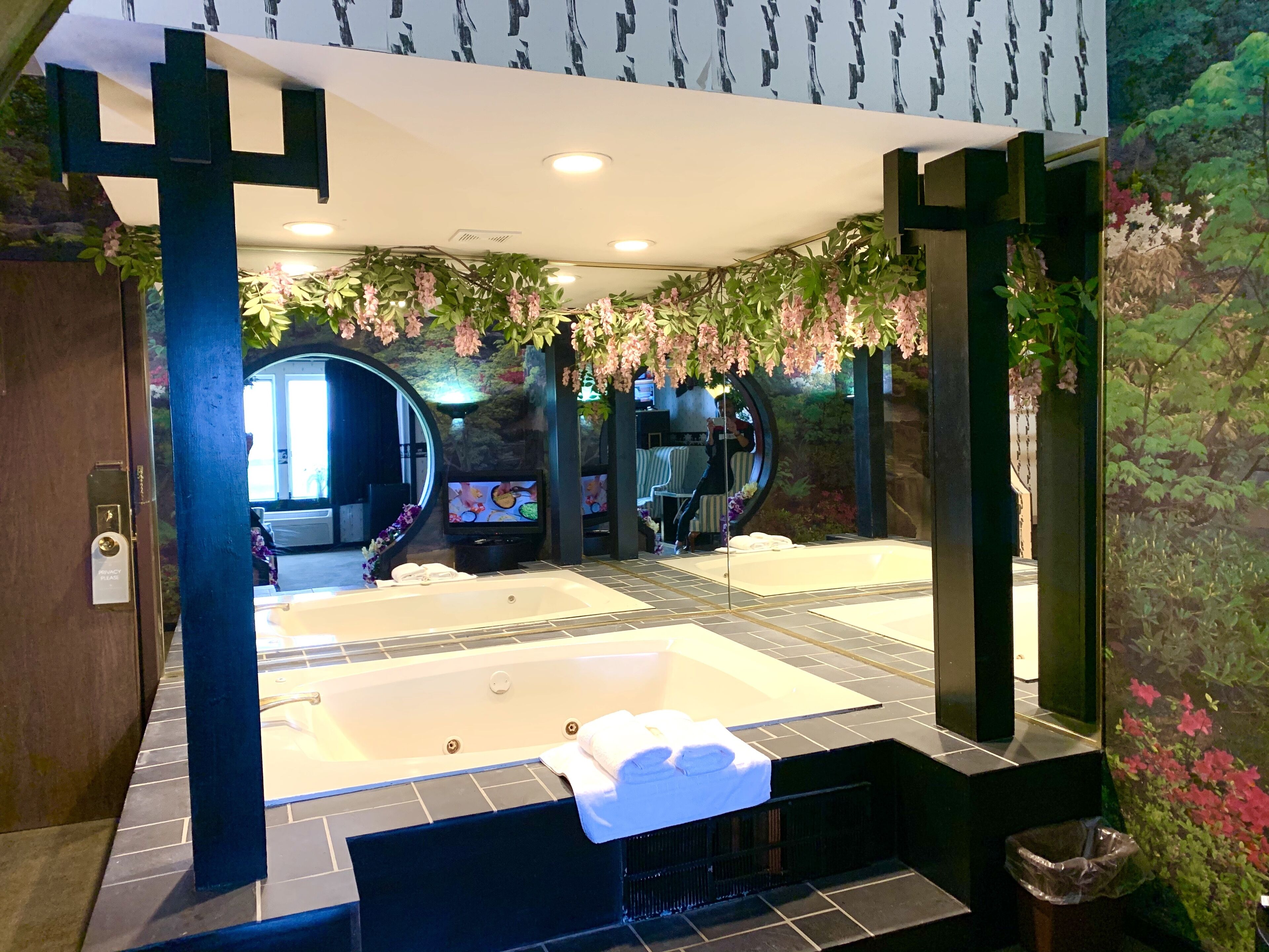 A spa area with a large hot tub, a seating area with a TV, and a decorative wall with hanging flowers.