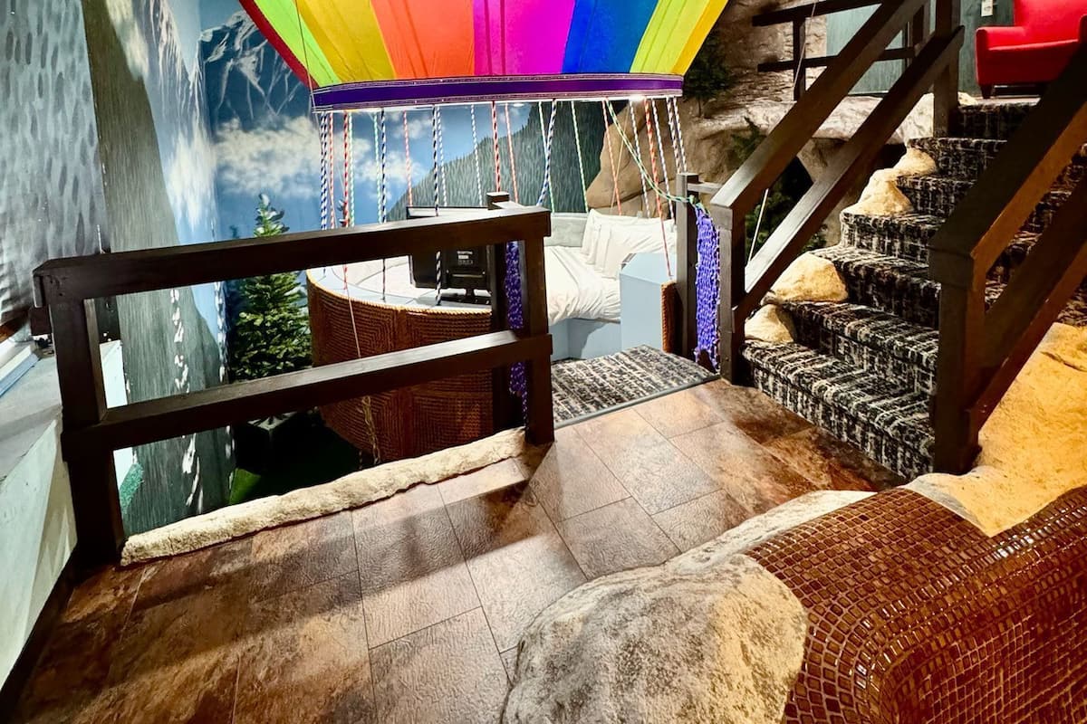 A room with a colorful hot air balloon decoration, a staircase, and a mural of mountains.