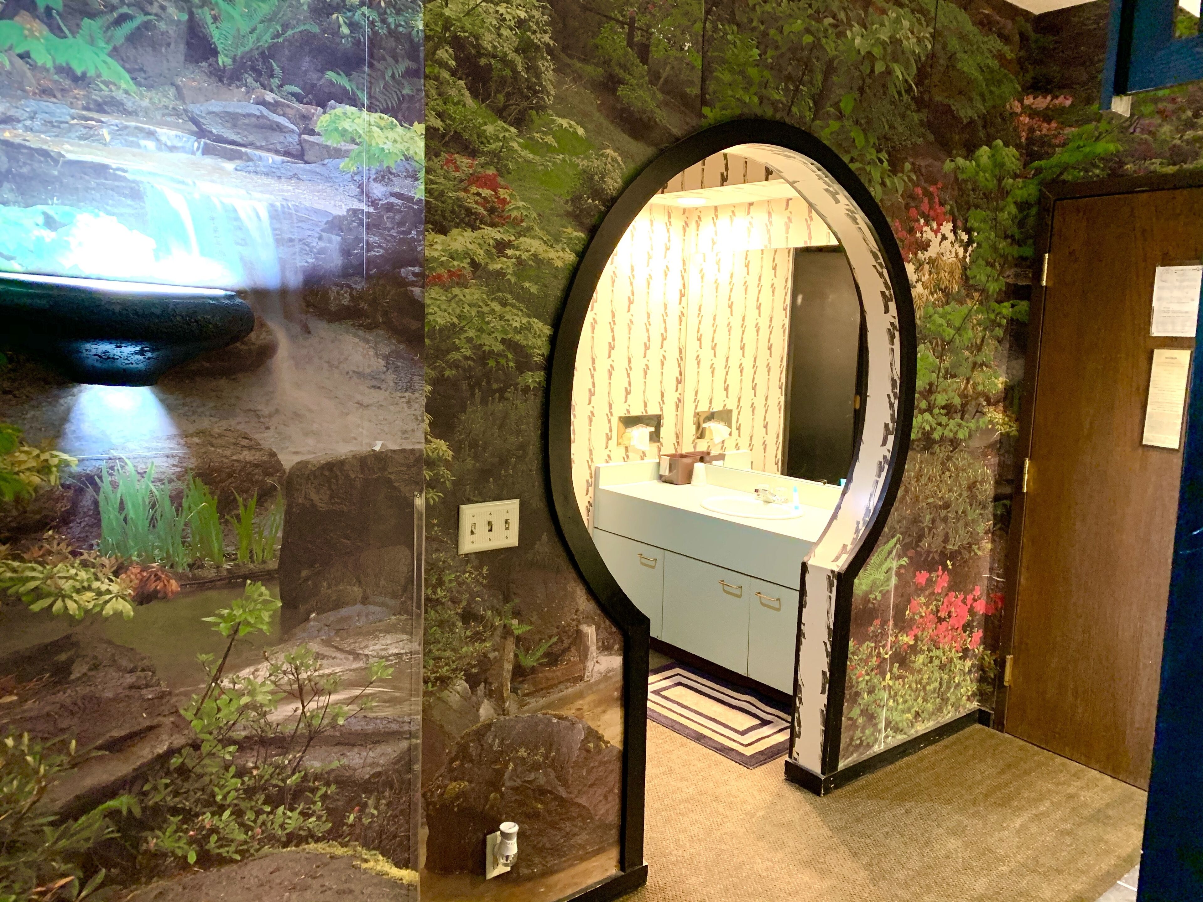 A bathroom with a waterfall mural, a round mirror, and a sink.
