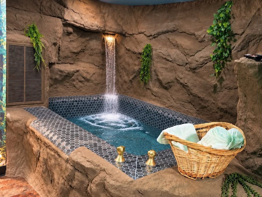 Un bain à remous doté d’une cascade, entouré de murs qui ressemblent à des rochers et de verdure.