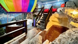 Una habitación con decoración de un globo aerostático colorido, una escalera con pared de roca y un mural de montañas.