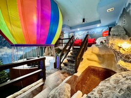 A room with a colorful hot air balloon decoration, a staircase with a rocky wall, and a mural of mountains.