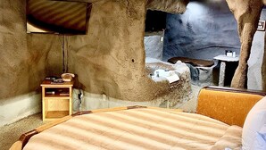 Un dormitorio con temática de cueva, que incluye una cama, un televisor y una pequeña mesa con un teléfono.