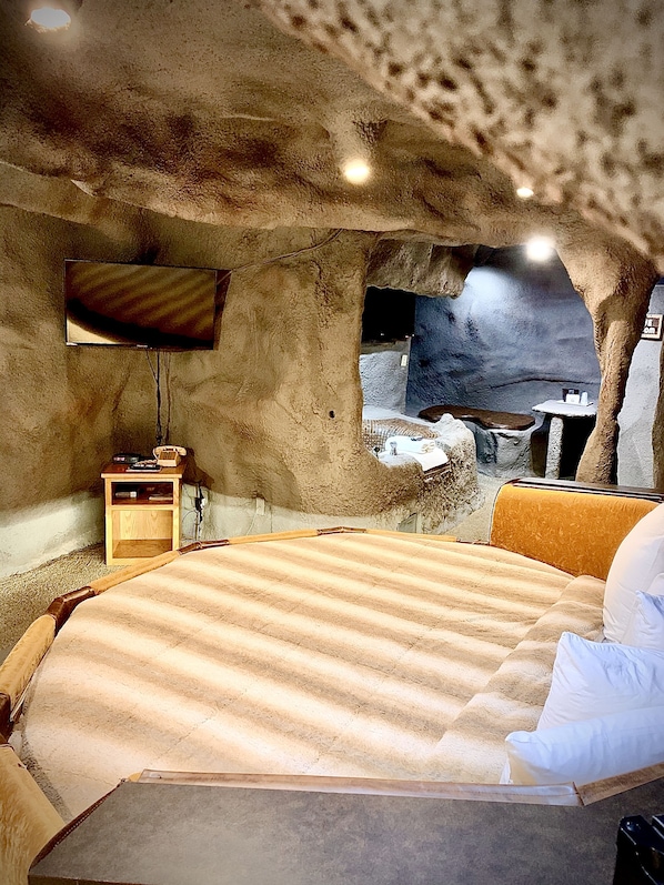 A cave-themed bedroom with a bed, a television, and a small table with a telephone.