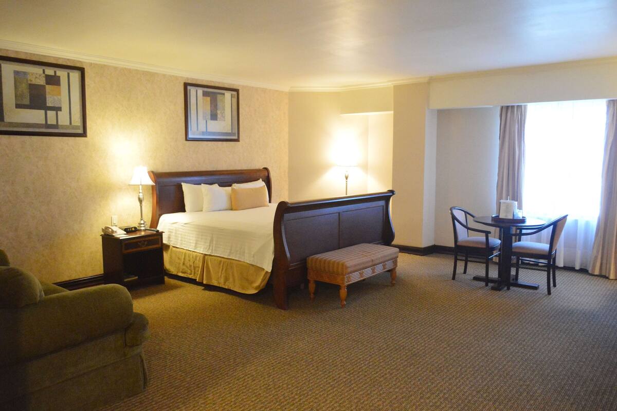 A hotel room with a bed, bedside table, lamp, chair, and a small table with chairs.