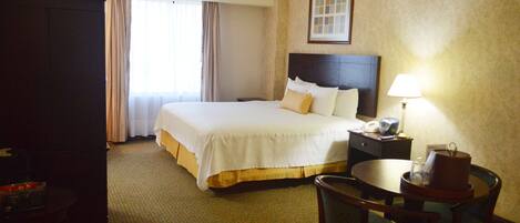 A hotel room with a large bed, a bedside table with a lamp, a chair, and a desk with a telephone.