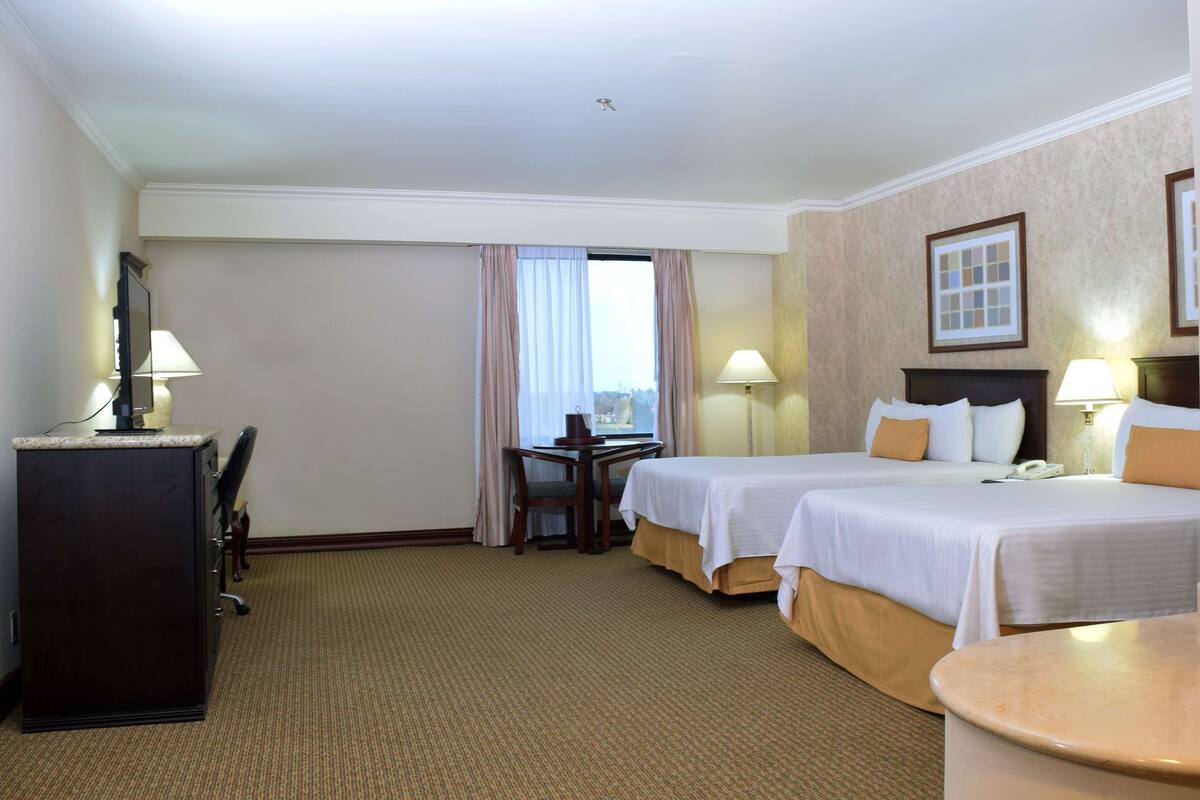 A hotel room with two beds, a desk, and a chair.