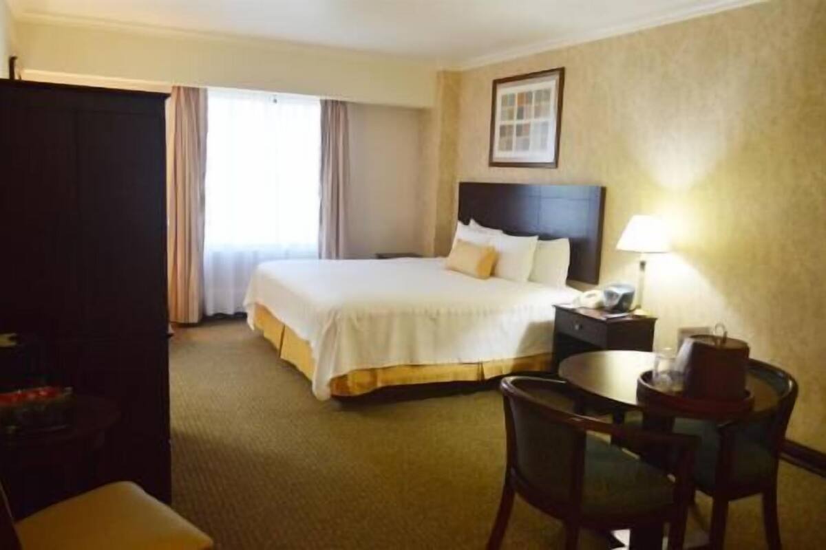 A hotel room with a bed, a desk, a chair, and a window with curtains.
