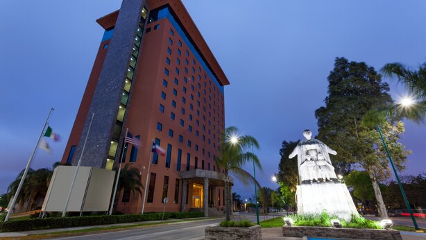 Et moderne hotel med en markant indgang, en statue og en velholdt have.