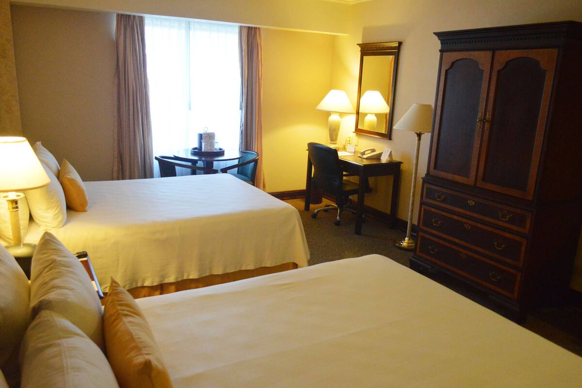 A hotel room with two beds, a desk, a chair, a lamp, a telephone, and a cabinet.