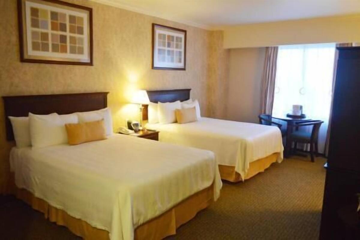A hotel room with two beds, a desk, a chair, and a window.