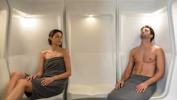 Deux personnes sont assises dans un espace aménagé comme un spa, avec des bancs et un éclairage suspendu.