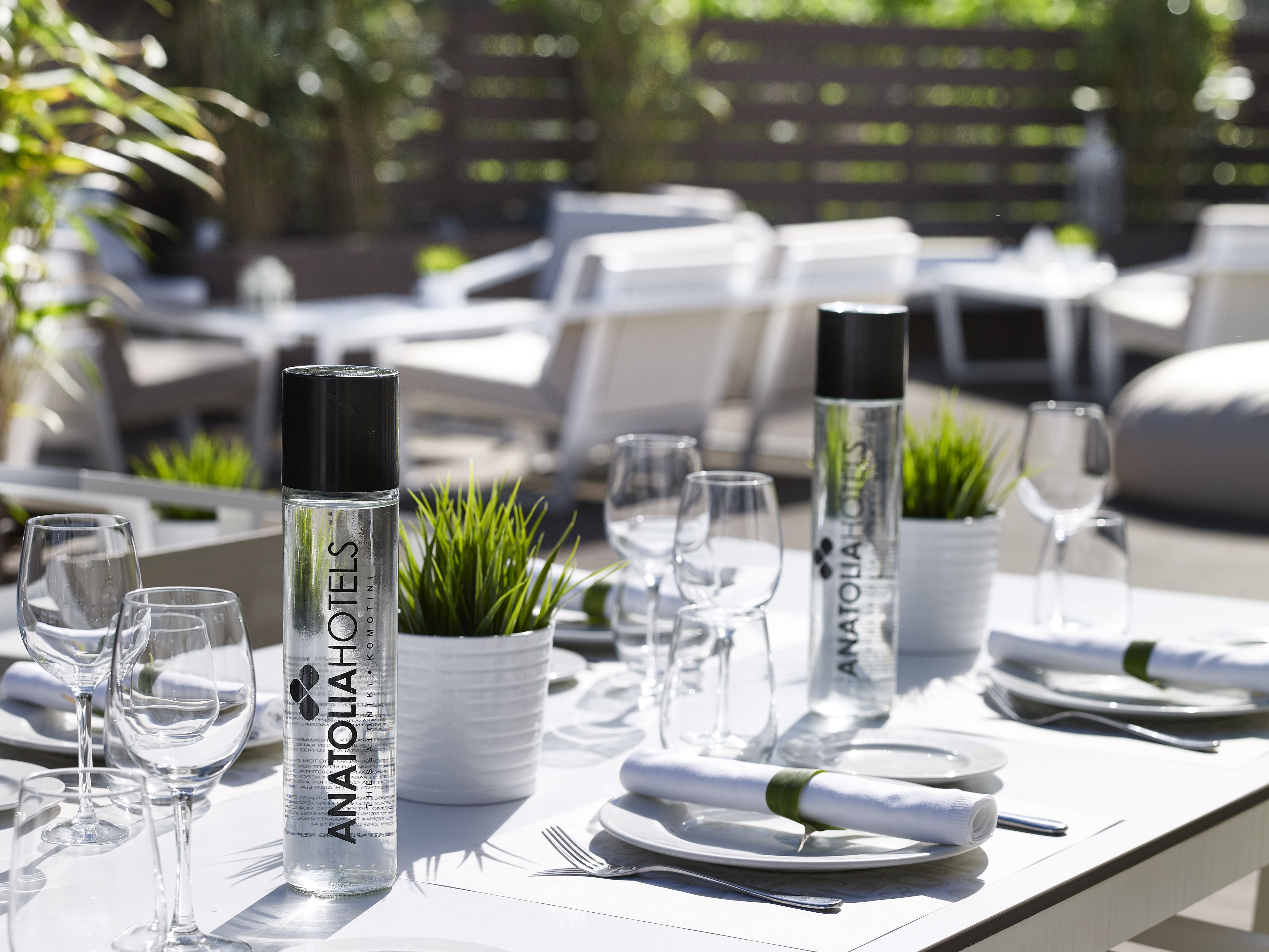 A table set with clear glassware, white plates, and a bottle labeled "ANATOLIA HOTELS".