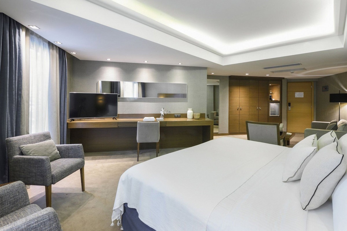 Una habitación de hotel con una cama grande, un escritorio con televisor de pantalla plana, una silla y un armario.